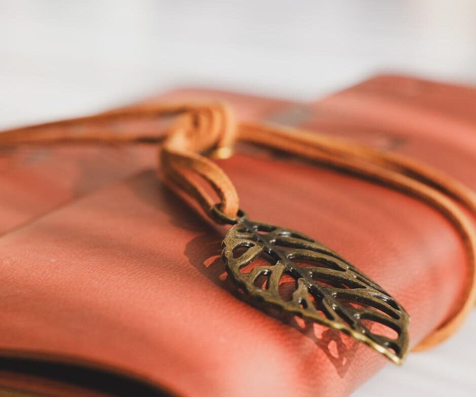Close-up of a leather-bound journal with a metal leaf bookmark elegantly wrapped in straps.