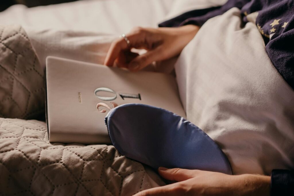 Close-up of a person holding a journal with a sleep mask on the bed, perfect for cozy nighttime routines.