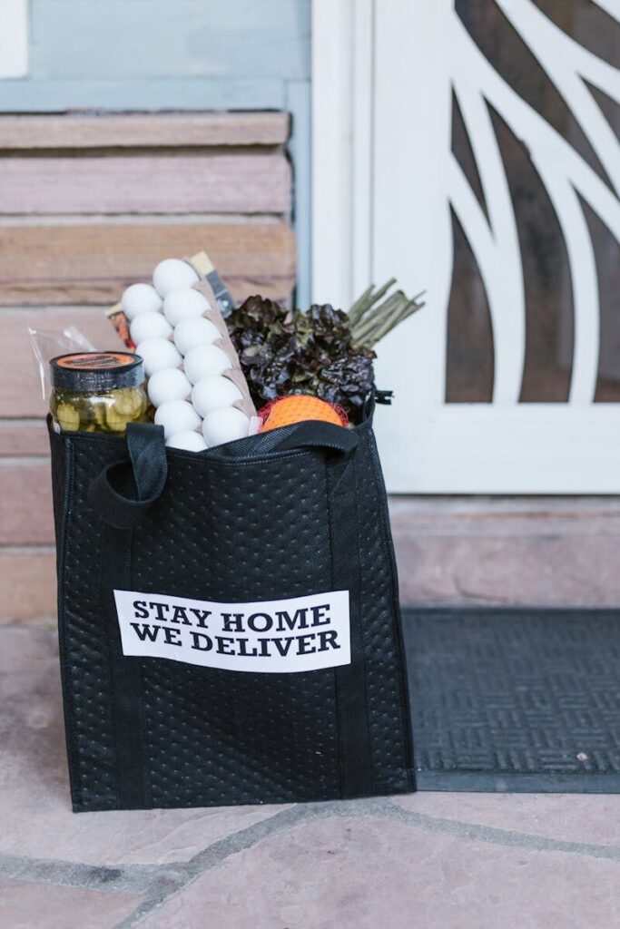 Reusable grocery bag with fresh produce and eggs on doorstep during stay-at-home delivery.