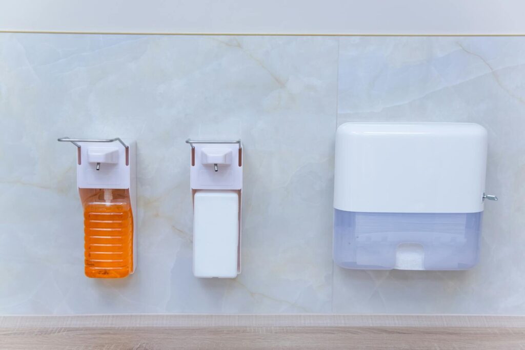 Close-up of wall-mounted soap, sanitizer, and paper dispenser in a sterile environment.