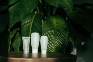 White cosmetic containers with green leaves backdrop, perfect for eco-friendly product representation.