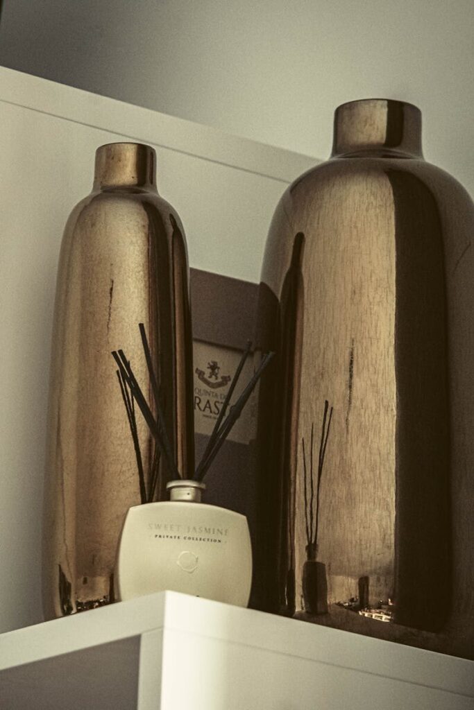 Sophisticated arrangement of metallic vases and sweet jasmine diffuser on a shelf.