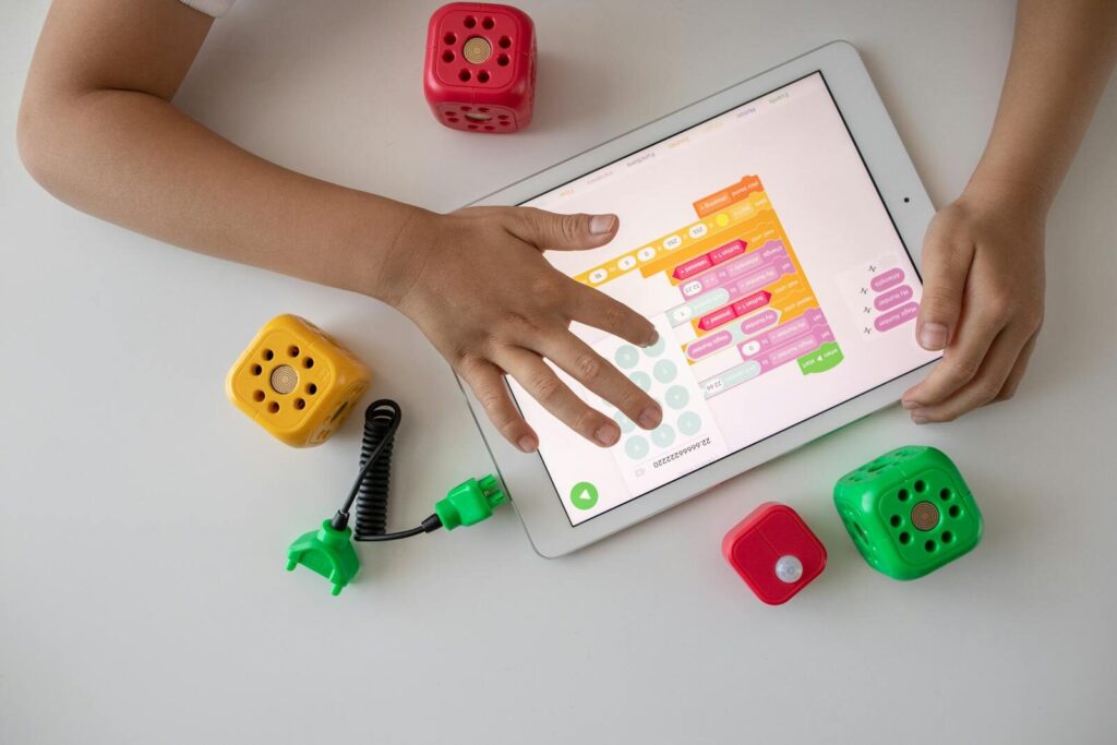 Child using digital tablet for coding education alongside colorful toy blocks.