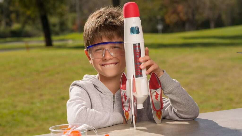 A smiling boy enjoys playing with a toy rocket on a sunny day.