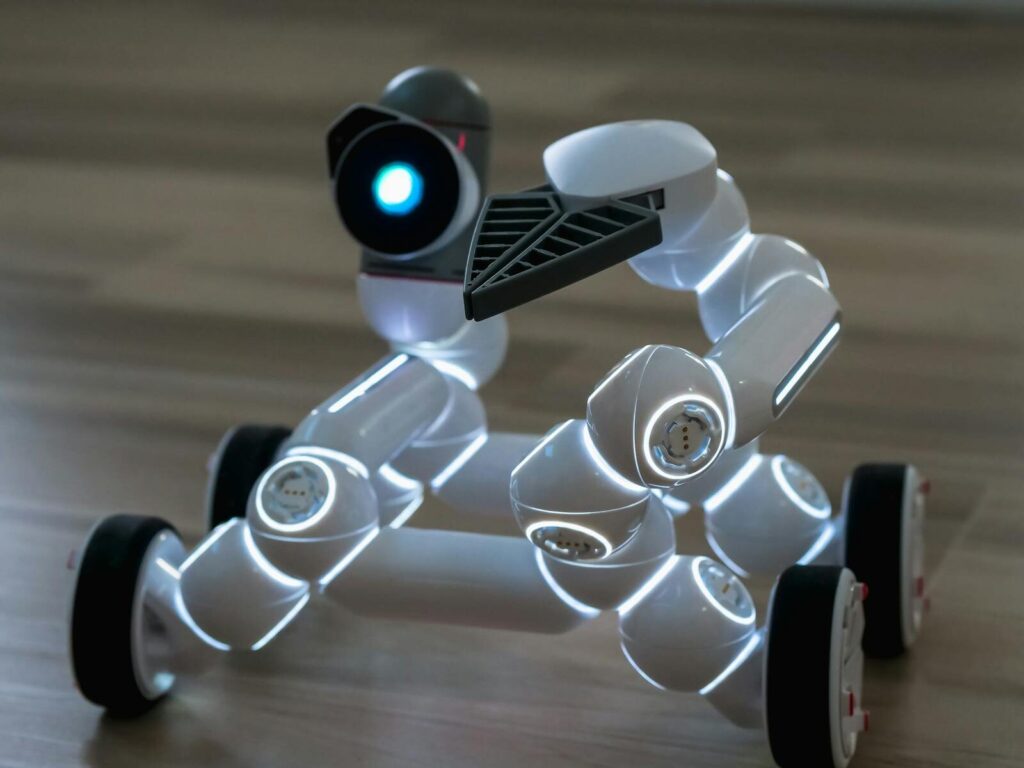Close-up of a wheeled robot toy with LED lights on a wooden floor indoors.