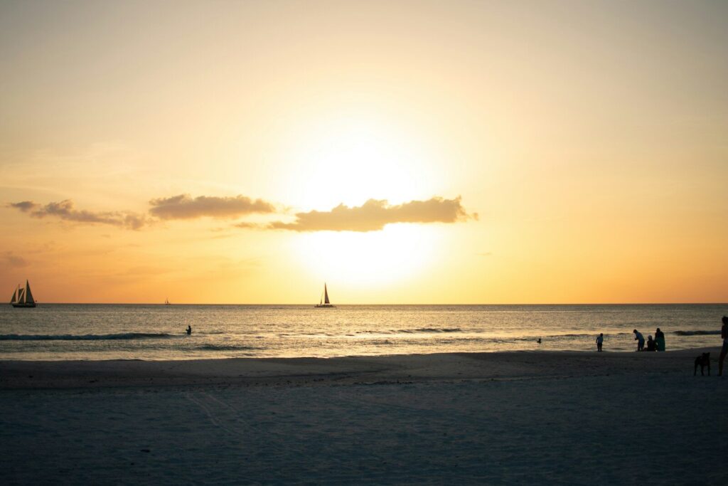 The sun is setting over the ocean with a sailboat in the distance