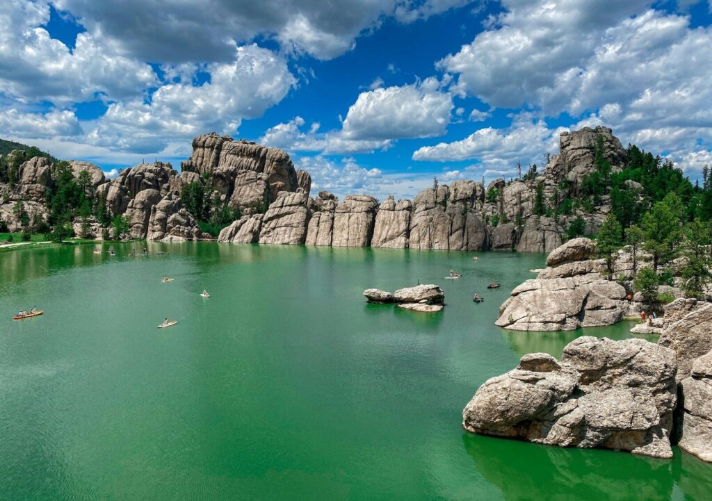 a body of water with rocks and trees around it with Sylvan Lake in the background