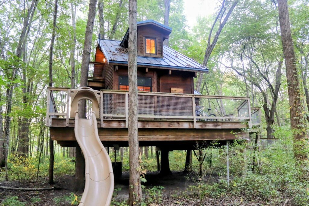 Wooden treehouse with slide in a forest setting.