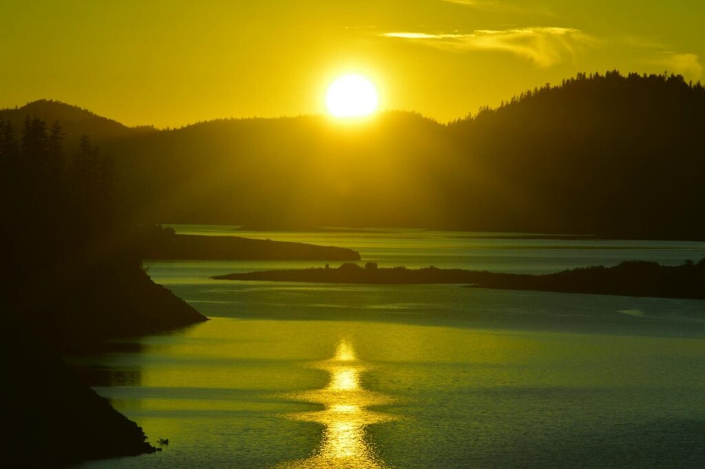 Breathtaking sunset over a calm lake, highlighting silhouettes of hilly landscapes.