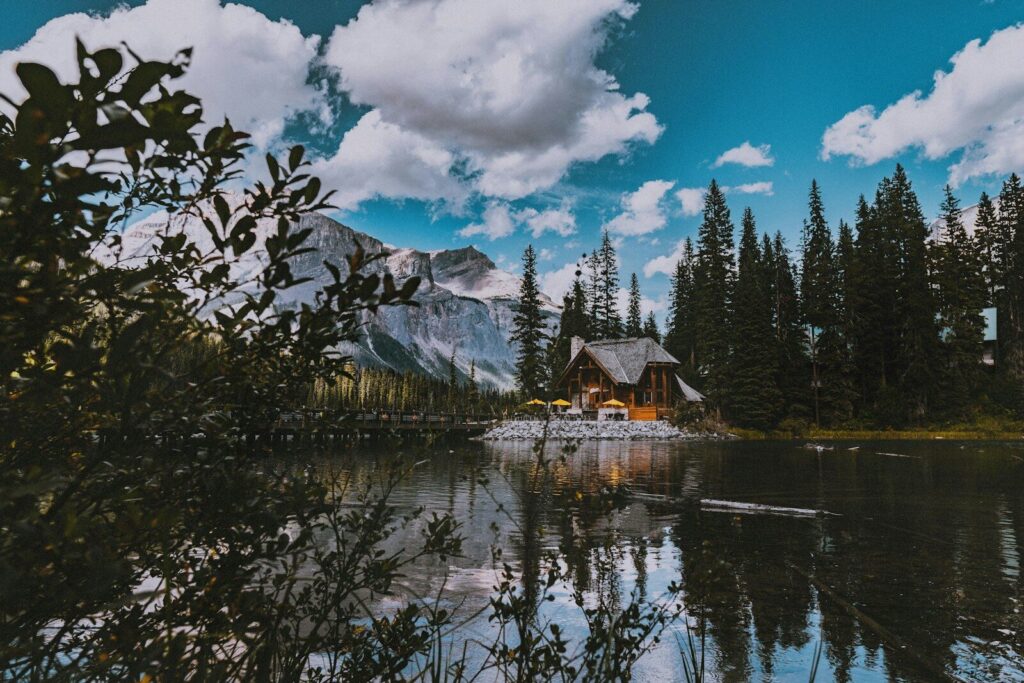 Cozy Cabin Getaways; brown wooden house near green trees and mountain under white clouds and blue sky during daytime