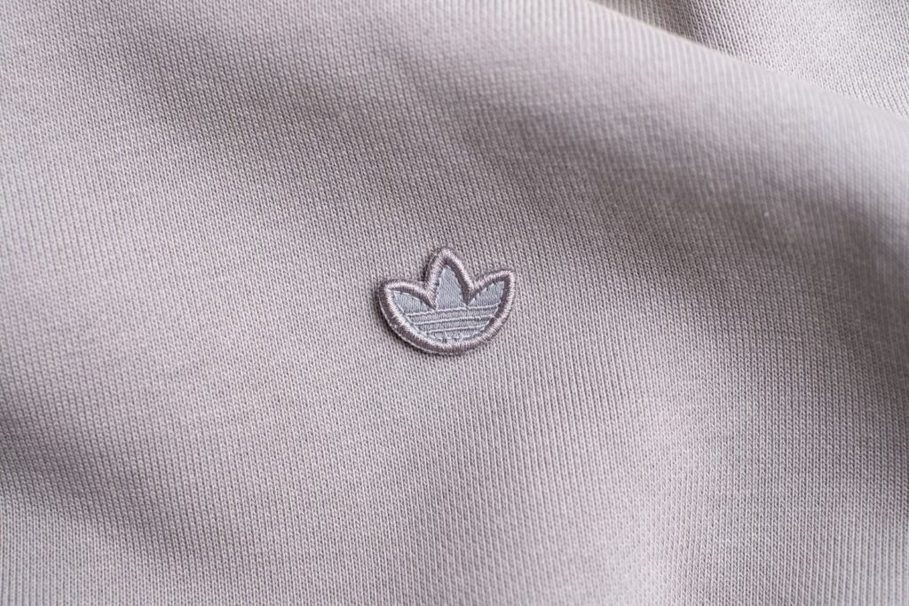 Eco-Friendly Fashion; Detailed view of fabric texture with an embroidered logo in a neutral color scheme.